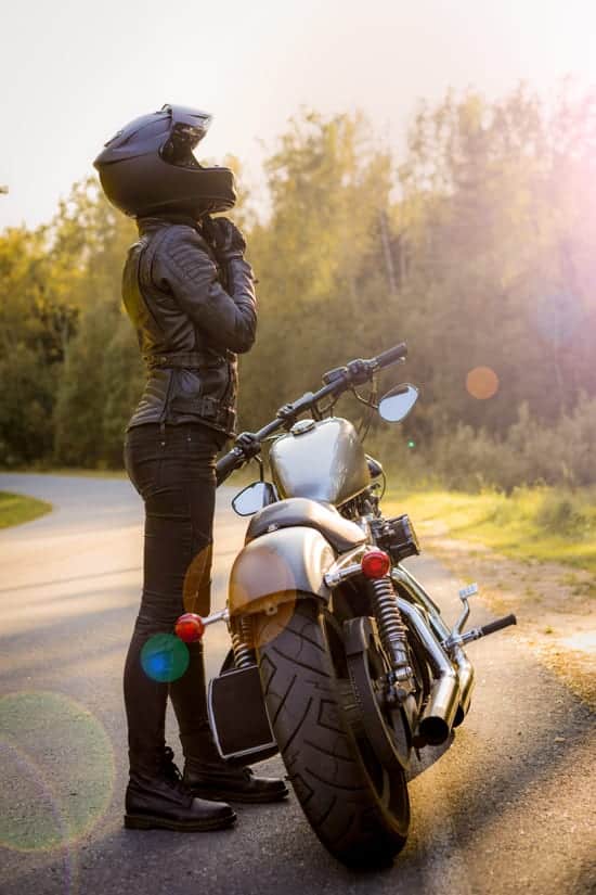 Motorcyclist Standing Near MotorCycle Adjusting Helmet Strap